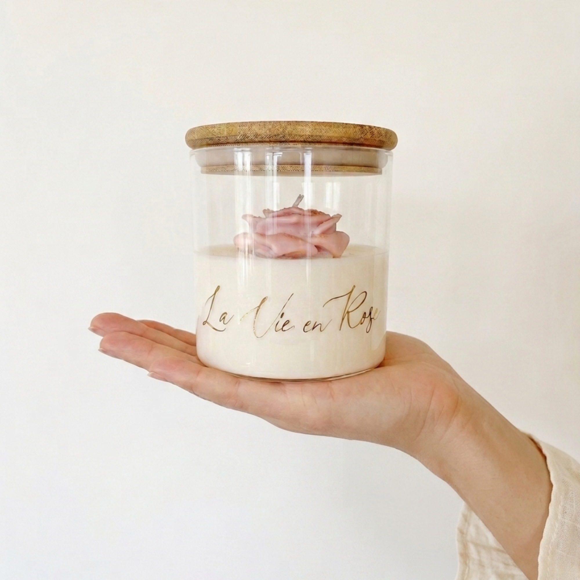 La Vie en Rose Rose Candle in glass jar with wooden lid, golden lettering and pink rose detail on top.
